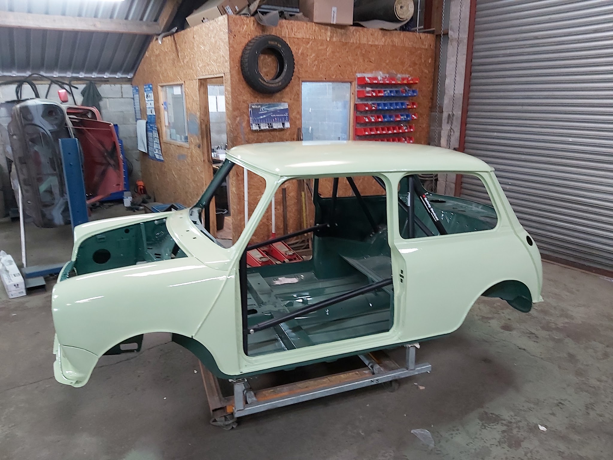 A classic Mini bodyshell in pale green on a frame in the workshop