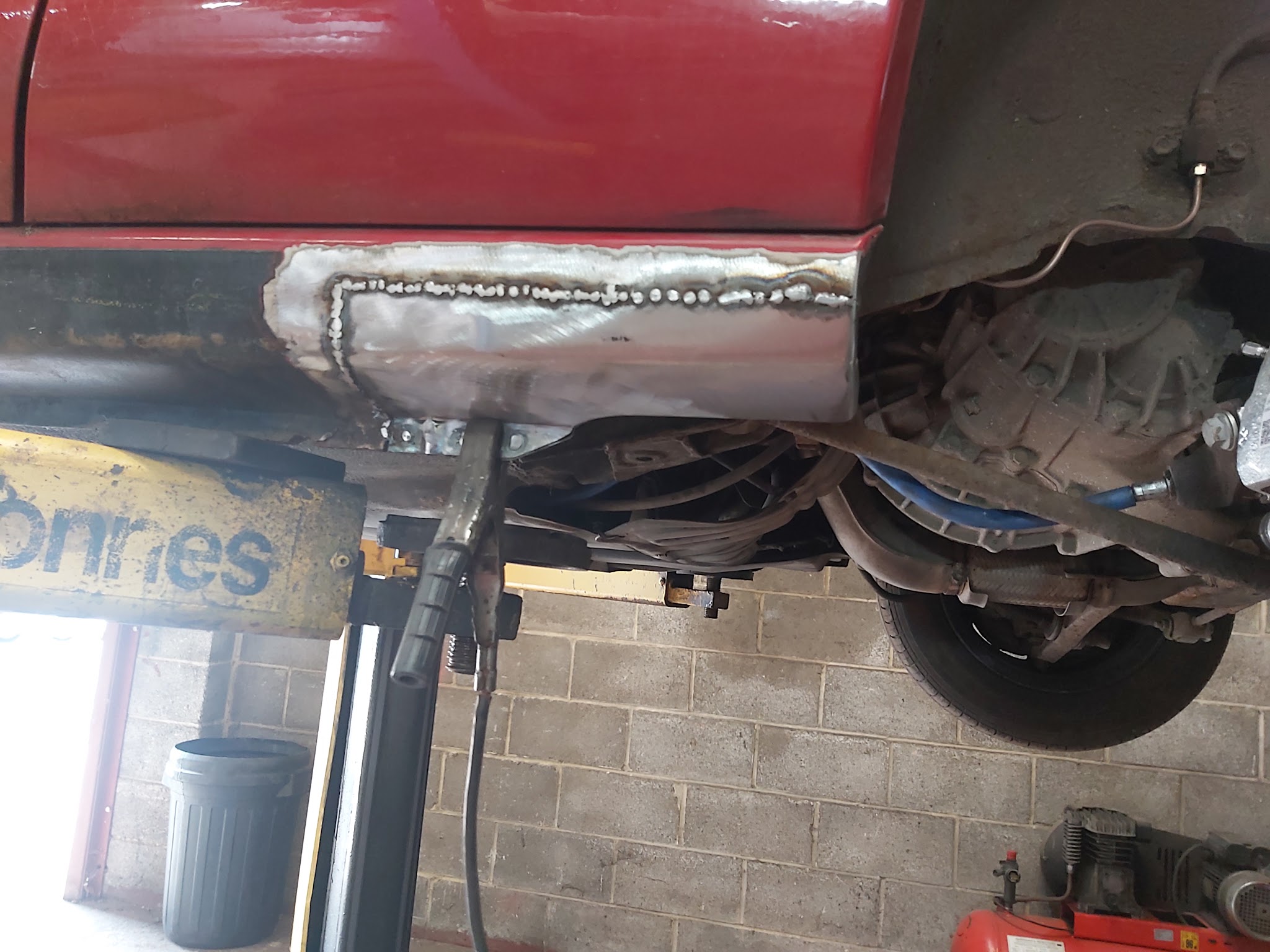 Fresh welding along the sill of a red car, seen from underneath on the lift